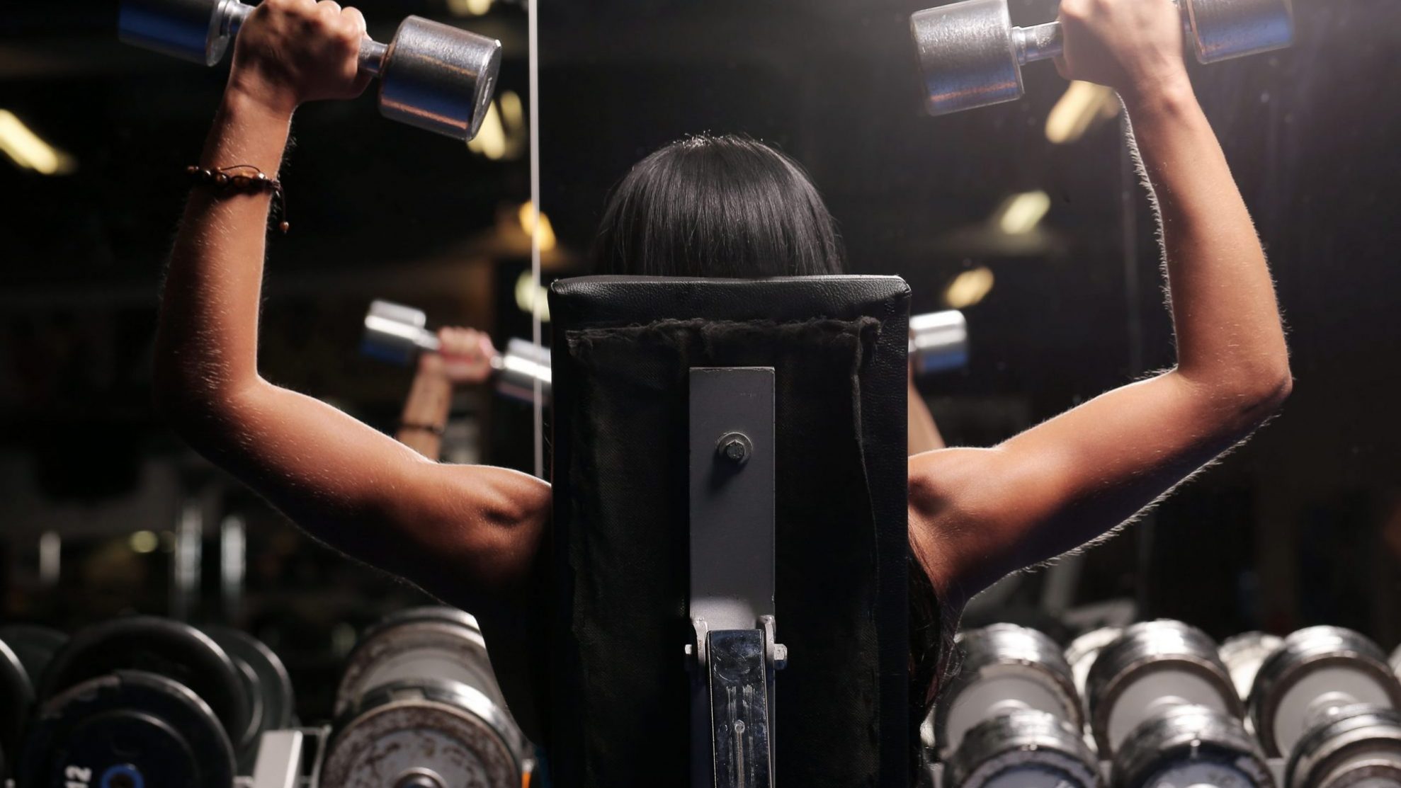 Muscular beautiful woman at a gym Photo of woman exercising with dumbbells illustrates blog: "Gyms Become Popular Tenants in the Post-Pandemic World"
