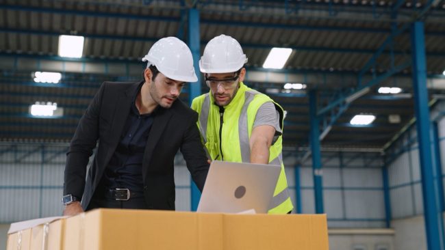 Warehouse workers looking at laptop illustrates blog "What Factors To Consider When Choosing a Warehouse?"