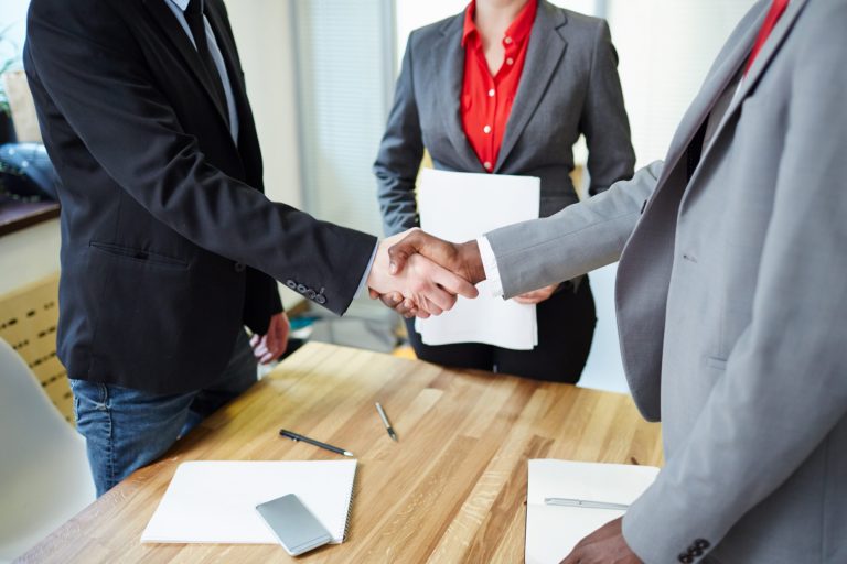 Photo of two men shaking hands with a woman in the background illustrates blog "What Is a Landlord Responsible for in a Triple Net Lease?"